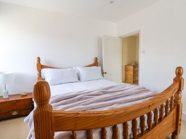 A bedroom with a wooden bed frame white pillows a blanket a wooden chest with a lamp and an open door showing a wooden dresser at Charmouth Lodge in Charmouth