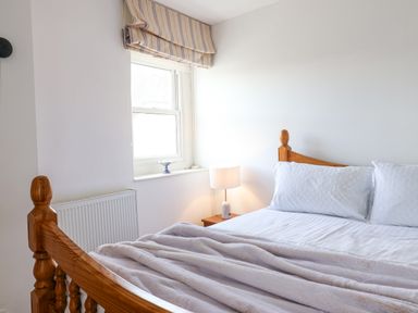A bedroom with a wooden bed frame bedside table with a lamp and a window with a striped roman shade at Charmouth Lodge in Charmouth