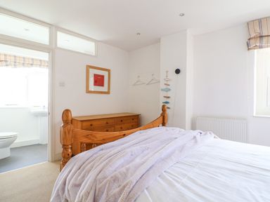A bedroom with a wooden bed frame and chest of drawers with access to a bathroom at Charmouth Lodge in Charmouth