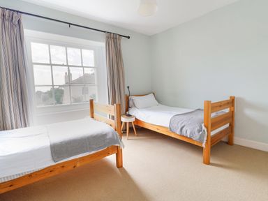 A bedroom with two wooden single beds a small round bedside table and a window with curtains at Charmouth Lodge in Charmouth