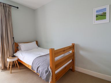 A bedroom with a single wooden bed a side table with a lamp and a framed picture on the wall at Charmouth Lodge in Charmouth