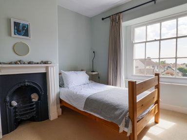 A bedroom with a wooden single bed beside a window and a fireplace at Charmouth Lodge in Charmouth