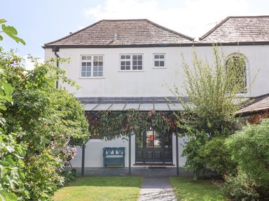 The back view of a two story house with a covered patio and garden in front at Charmouth Lodge in Charmouth