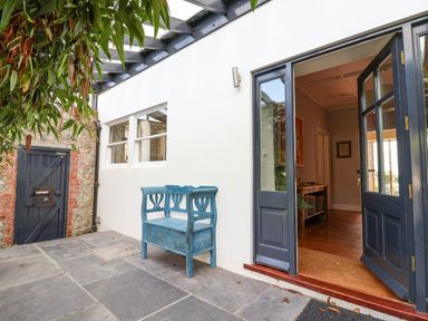 An outdoor patio area with a blue bench under a pergola and a dark wood door open to a room at Charmouth Lodge in Charmouth