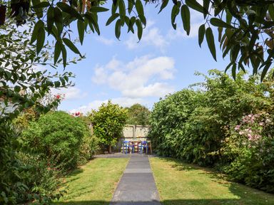 A garden with a stone pathway leading to a table and chairs surrounded by greenery and flowers at Charmouth Lodge in Charmouth