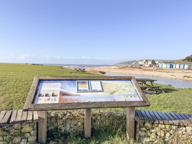 An information board about Charmouth Beach with a grassy area picnic tables and pebble beach at Charmouth Lodge in Charmouth