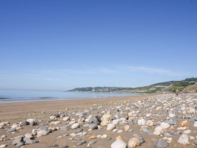 A rocky beach with sand and scattered stones with hills and buildings in the background at Charmouth Lodge in Charmouth