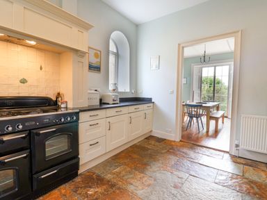 A kitchen with a black stove white cabinets a toaster and a dining room visible through a doorway at Charmouth Lodge in Charmouth