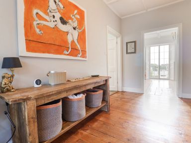 A hallway with a wooden console table baskets and a lamp under a painting and a view into a room with large windows at Charmouth Lodge in Charmouth