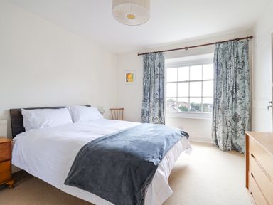 A bedroom with a bed a wooden nightstand a wooden dresser and patterned curtains at Charmouth Lodge in Charmouth