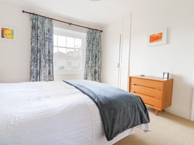 A bedroom with a large window with patterned curtains a double bed and a wooden dresser at Charmouth Lodge in Charmouth