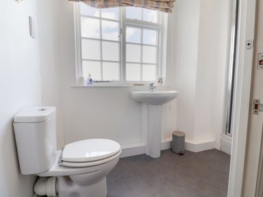 A bathroom with a toilet sink window and small trash can at Charmouth Lodge in Charmouth