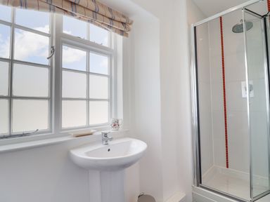 A bathroom with a sink under a window and a glass shower enclosure at Charmouth Lodge in Charmouth