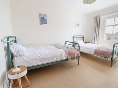 A bedroom with two single beds with green metal frames a small round wooden table and windows at Charmouth Lodge in Charmouth