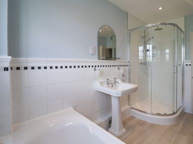 A bathroom with a white bathtub pedestal sink mirror and glass shower enclosure at Charmouth Lodge in Charmouth