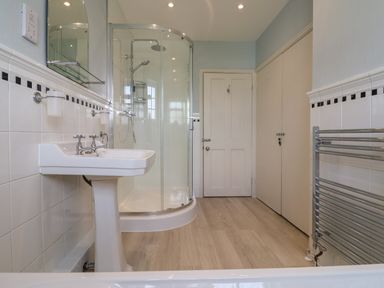 A bathroom with a pedestal sink and glass shower enclosure and a white door and towel rack at Charmouth Lodge in Charmouth