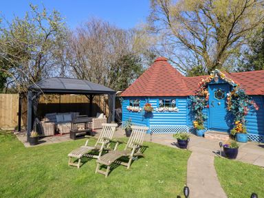 A garden with two wooden lounge chairs a blue cabin with a red roof and a gazebo with seating at Applejacks Orchard in Holywell
