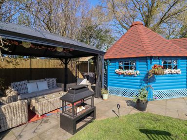 An outdoor seating area with wicker furniture under a canopy a small blue building with flower boxes under the windows and a red shingled roof at Applejacks Orchard in Holywell