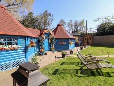A blue garden house with red roof tiles and flower decorations in a garden with lawn chairs and a wooden shed at Applejacks Orchard in Holywell