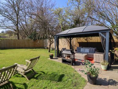 A garden with wooden chairs on the grass and a covered outdoor seating area with wicker furniture and a fire pit at Applejacks Orchard in Holywell