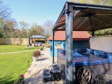 An outdoor area with a hot tub under a gazebo a blue wooden shed and a seating area under another gazebo at Applejacks Orchard in Holywell