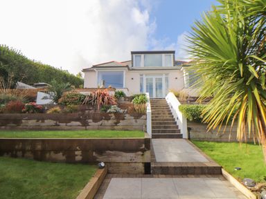 A house with stairs leading up to a patio garden with plants and lawn at Higher Bolenna in Perranporth