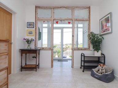 A hallway with a wooden table with flowers on the left a plant on a black metal cart on the right and a dog in a bed at Higher Bolenna in Perranporth