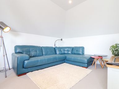 A living room with a blue sectional sofa white rug standing lamp small tables and a plant at Higher Bolenna in Perranporth