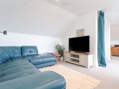 A living room with a blue sectional sofa a beige TV stand with a flat screen TV and a cream rug at Higher Bolenna in Perranporth