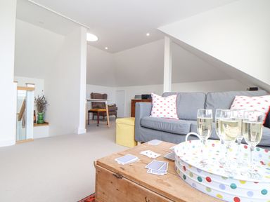 A living room with a grey sofa pillows wooden table with drinks and cards and an armchair at Higher Bolenna in Perranporth