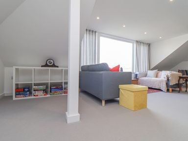 A living room with sofas a yellow ottoman a shelf with board games and a clock at Higher Bolenna in Perranporth