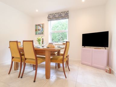 A dining area with a wooden table and yellow chairs next to a window and a television on a cabinet at Higher Bolenna in Perranporth