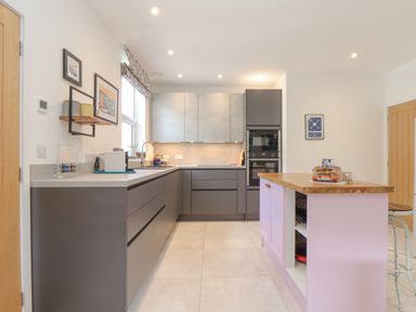 A kitchen with grey cabinets a pink island wooden countertop and appliances at Higher Bolenna in Perranporth