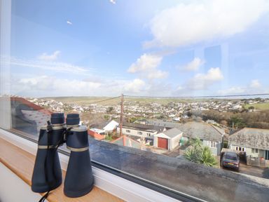 Binoculars on a windowsill looking out over a town with houses and hills at Higher Bolenna in Perranporth