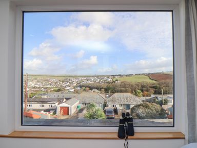 A window view showing rooftops trees and hills with a pair of binoculars on the windowsill at Higher Bolenna in Perranporth