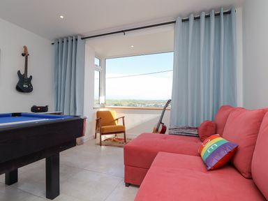 A room with a pool table guitar on the wall yellow chair and red sofa with colorful pillow at Higher Bolenna in Perranporth