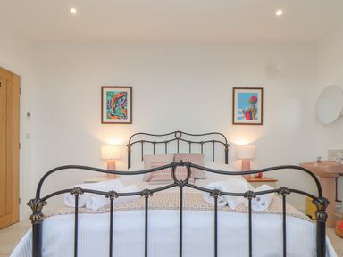 A bedroom with a black metal bed frame two bedside tables with lamps and rolled towels on the bed at Higher Bolenna in Perranporth