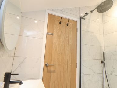 A bathroom with a wooden door a round mirror tiled walls a black faucet and a showerhead at Higher Bolenna in Perranporth