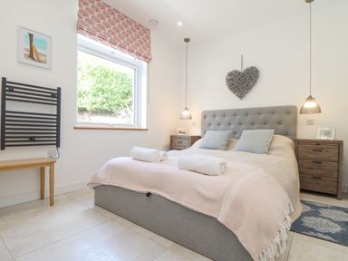 A bedroom with a grey upholstered bed and rolled towels on the bed at Higher Bolenna in Perranporth