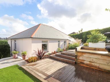 An outdoor garden area with wooden decking steps plants and a section of a house at Higher Bolenna in Perranporth