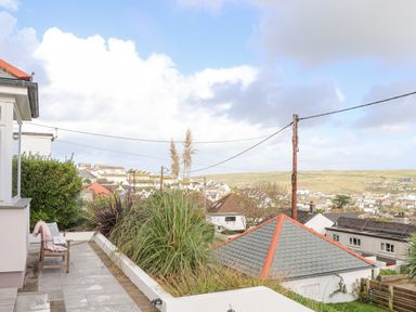 A patio with a wooden chair and plants overlooking rooftops and hills at Higher Bolenna in Perranporth