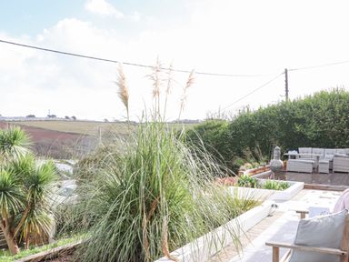 An outdoor patio area with seating and plants with fields in the background at Higher Bolenna in Perranporth