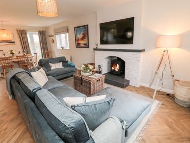 A living room with gray sofas a wicker coffee table a lit fireplace and a dining area at Driftwood Sands in Beadnell