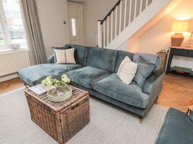 A living room with a blue sectional sofa and a wicker coffee table at Driftwood Sands in Beadnell