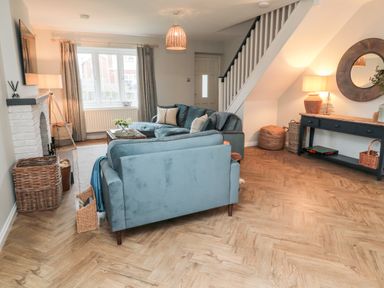 A living room with blue sofas a wooden floor a white brick fireplace and a black console table at Driftwood Sands in Beadnell