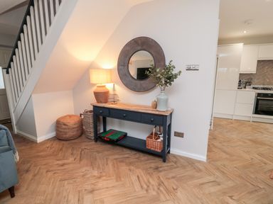 A hallway with a console table a round mirror and a lamp next to a staircase at Driftwood Sands in Beadnell