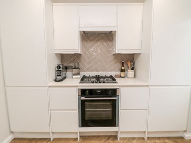 A kitchen with white cabinets a gas stove an oven knife block coffee machine and kitchen utensils at Driftwood Sands in Beadnell