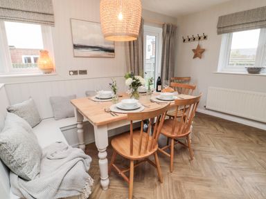 A dining area with a wooden table set for four with chairs and bench seating at Driftwood Sands in Beadnell