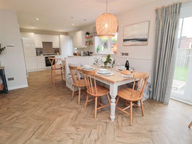 A dining table with wooden chairs and tableware in an open kitchen with white cabinets and a pendant light at Driftwood Sands in Beadnell