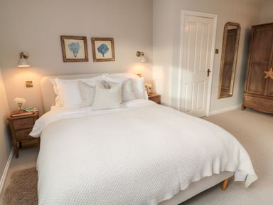 A bedroom with a bed made with white bedding a wooden wardrobe and mirror at Driftwood Sands Beadnell